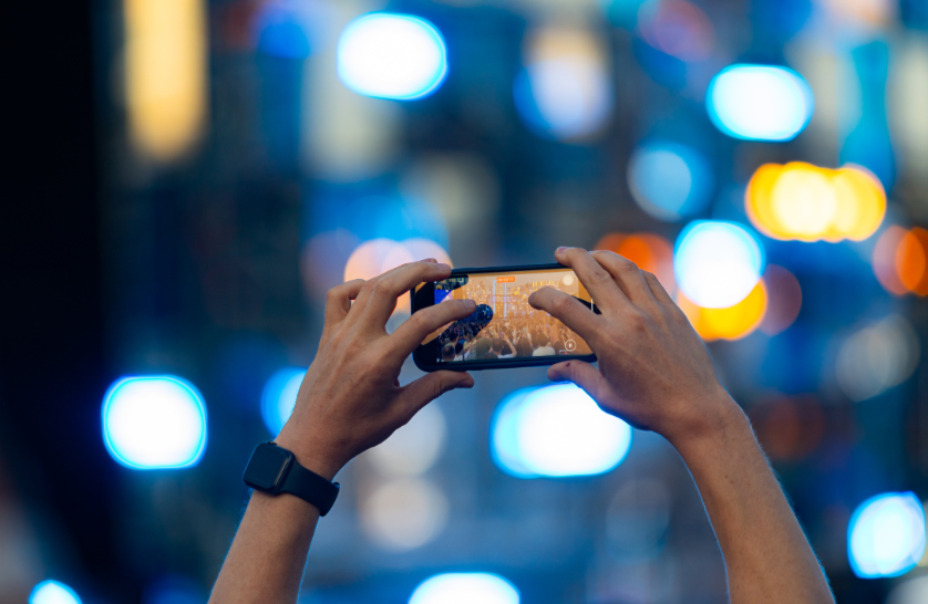 An image of hands holding up a phone to record at a concert